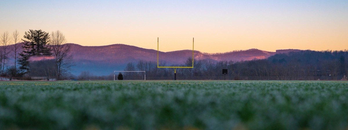 An empty football field at dawn with the goal post against purple hills