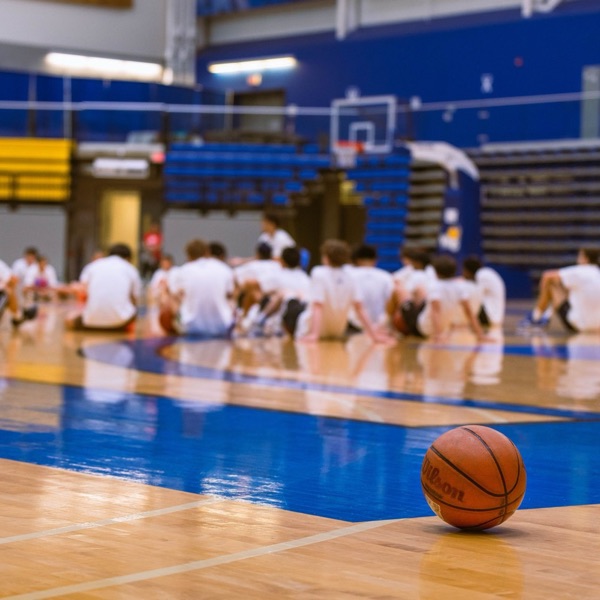 A basketball on the court with a youth team seated behind it listening to coaches
